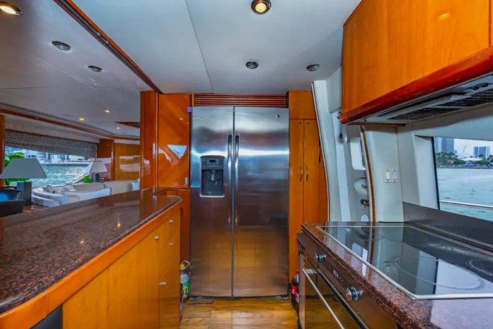 Modern yacht kitchen with stainless steel fridge, countertops, and city view through window.