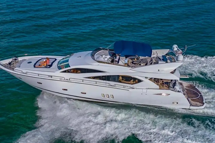 A white yacht cruising on the ocean with a sunbather on deck.