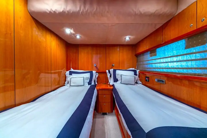 Two single beds in a wood-paneled room with blue and white bedding, central nightstand and overhead lights.