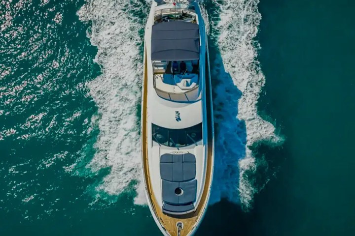Aerial view of a white yacht with dark canopies cruising on blue ocean water.