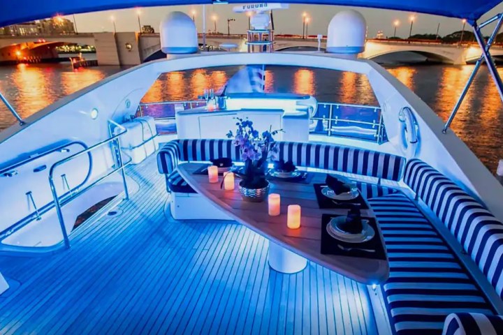 Luxury yacht deck with striped seating, table, candles, and evening city waterfront view.