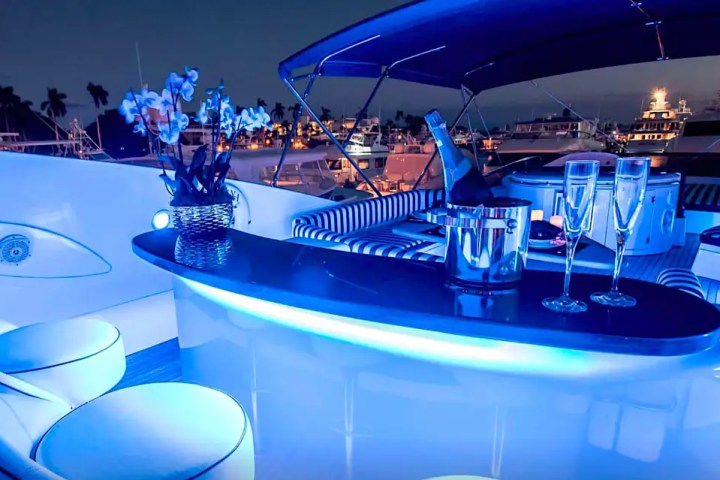 Luxurious yacht deck with blue lighting, table, champagne, and orchids at night.