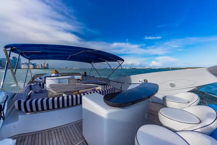 Luxury yacht deck with striped seating, blue canopy, and ocean view under a blue sky.
