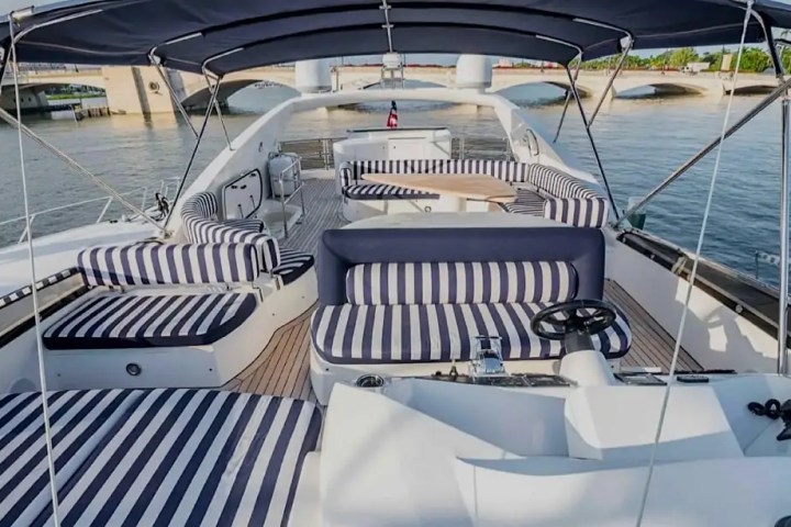 Luxurious yacht deck with striped seating and canopy, overlooking a bridge and calm water.