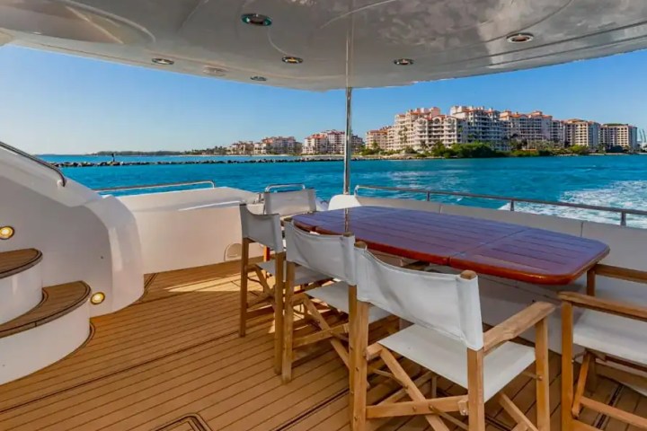 Deck of a yacht with table and chairs, overlooking a cityscape and blue ocean.
