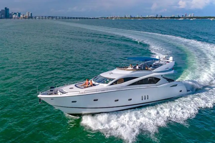 Luxury yacht cruising on blue water with city skyline in the background.