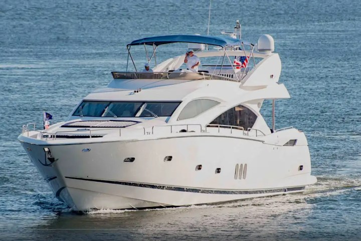 White yacht with blue canopy sailing on open water, flags on display.