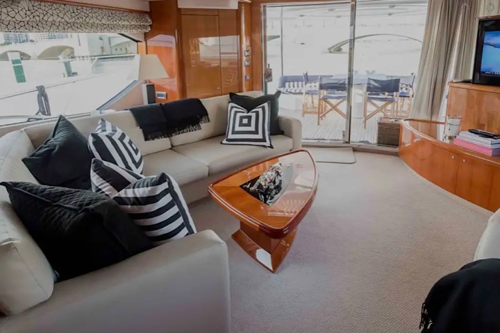 Luxury boat interior with cream sofas, black cushions, glass table, and TV.