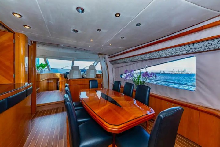 Luxurious yacht interior with wooden dining table, black chairs, and large windows showing ocean view.