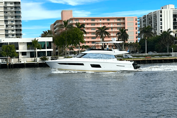 White yacht cruising on a canal with buildings and palm trees in the background.