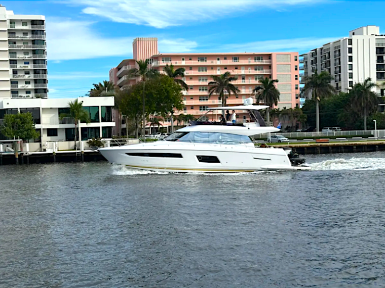 White yacht cruising on a canal with buildings and palm trees in the background.