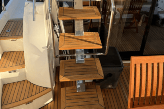 Wooden steps and railing on a boat deck with a table and chairs.