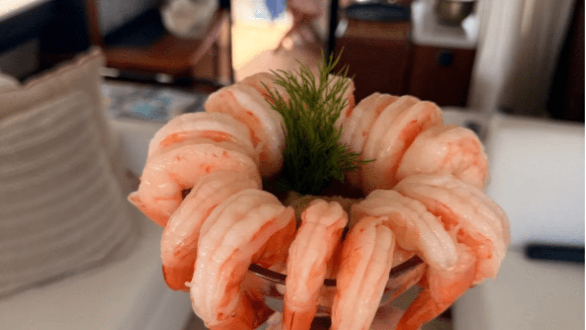 Hand holding shrimp cocktail on a boat with ocean view in background.