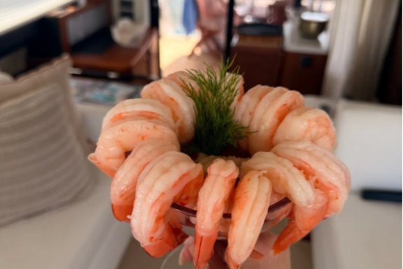 Hand holding shrimp cocktail on a boat with ocean view in background.