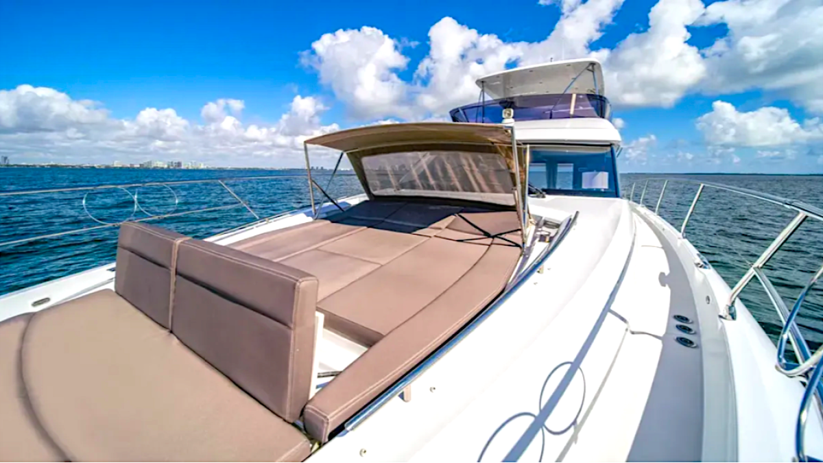 Deck of a yacht with cushioned seating under a canopy on a sunny day with ocean and clouds.