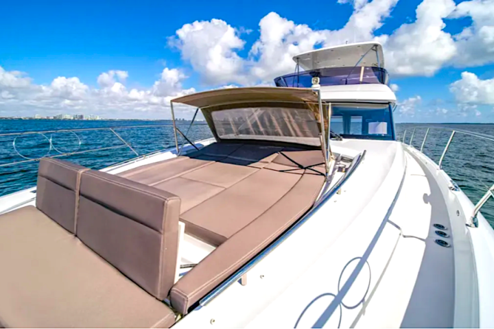 Deck of a yacht with cushioned seating under a canopy on a sunny day with ocean and clouds.