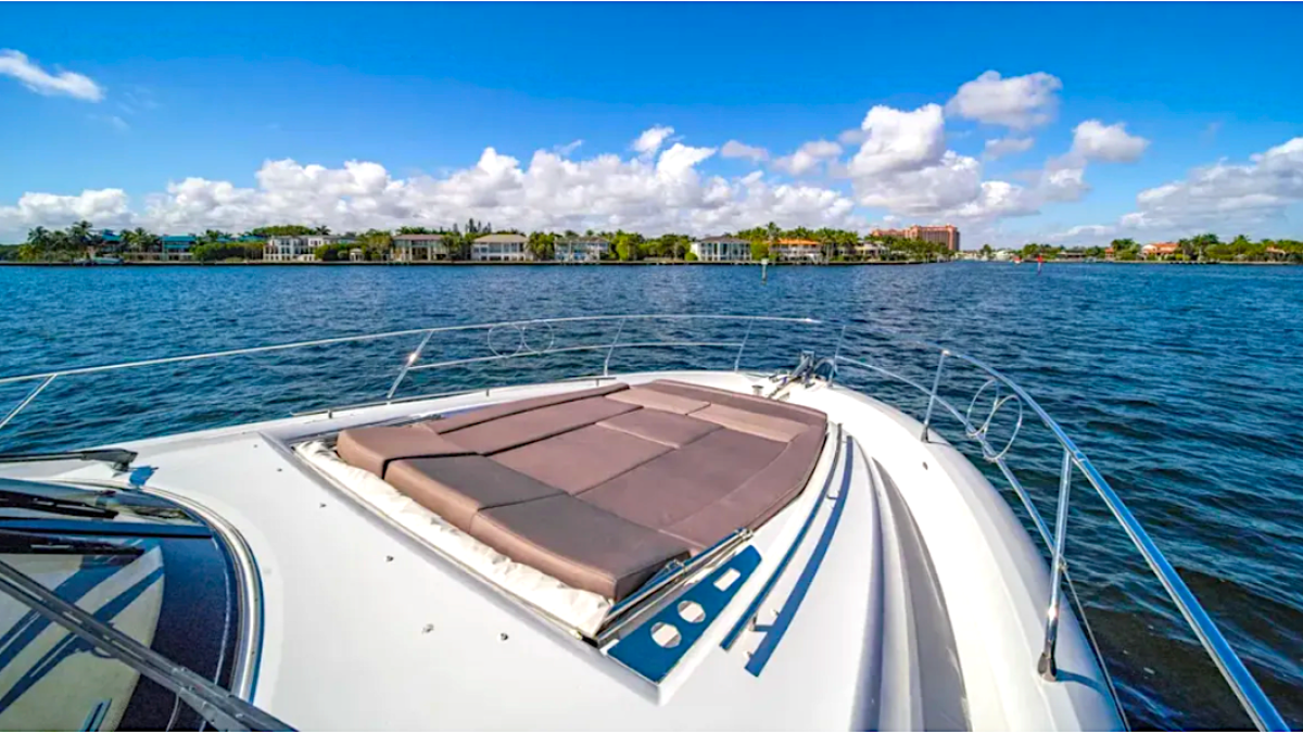 View from boat deck over water with buildings and trees in the distance under a blue sky with clouds.