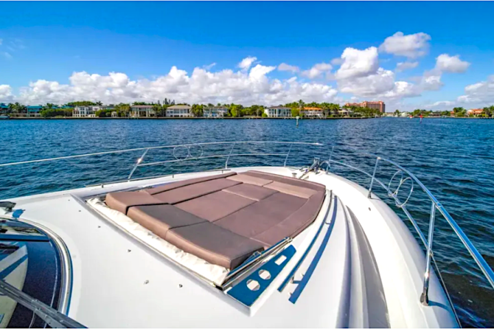 View from boat deck over water with buildings and trees in the distance under a blue sky with clouds.