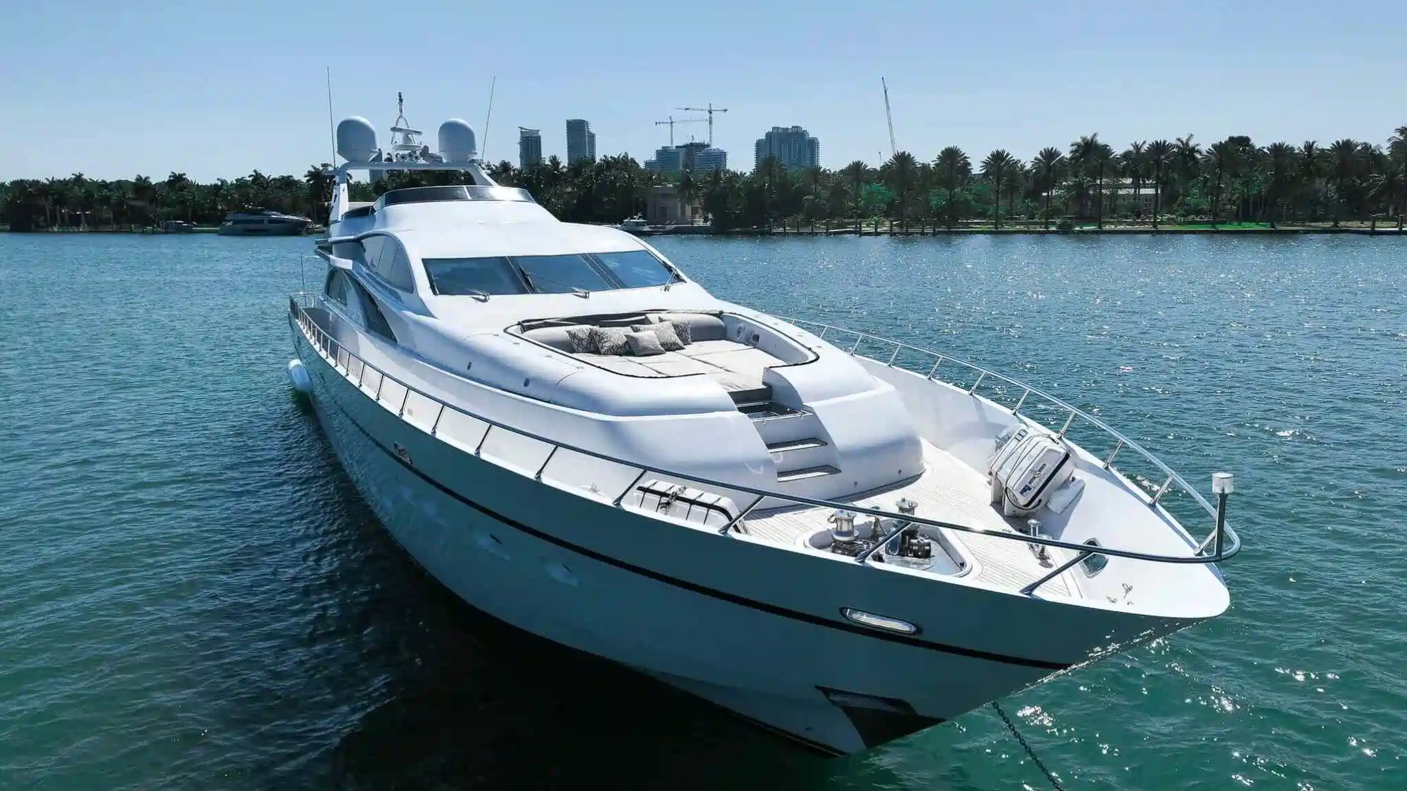 Large white yacht on water with city skyline and palm trees in background.