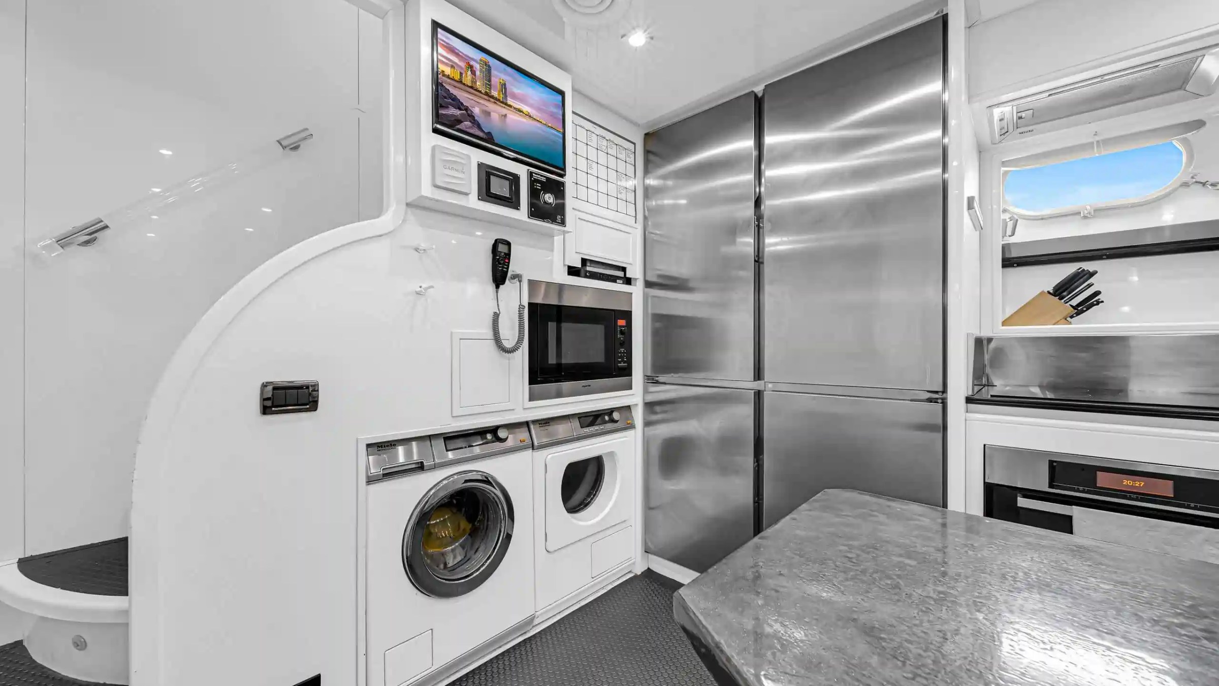 Modern kitchen area with stainless appliances, washer, dryer, and knife set by a small window.