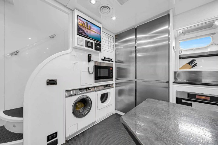 Modern kitchen area with stainless appliances, washer, dryer, and knife set by a small window.