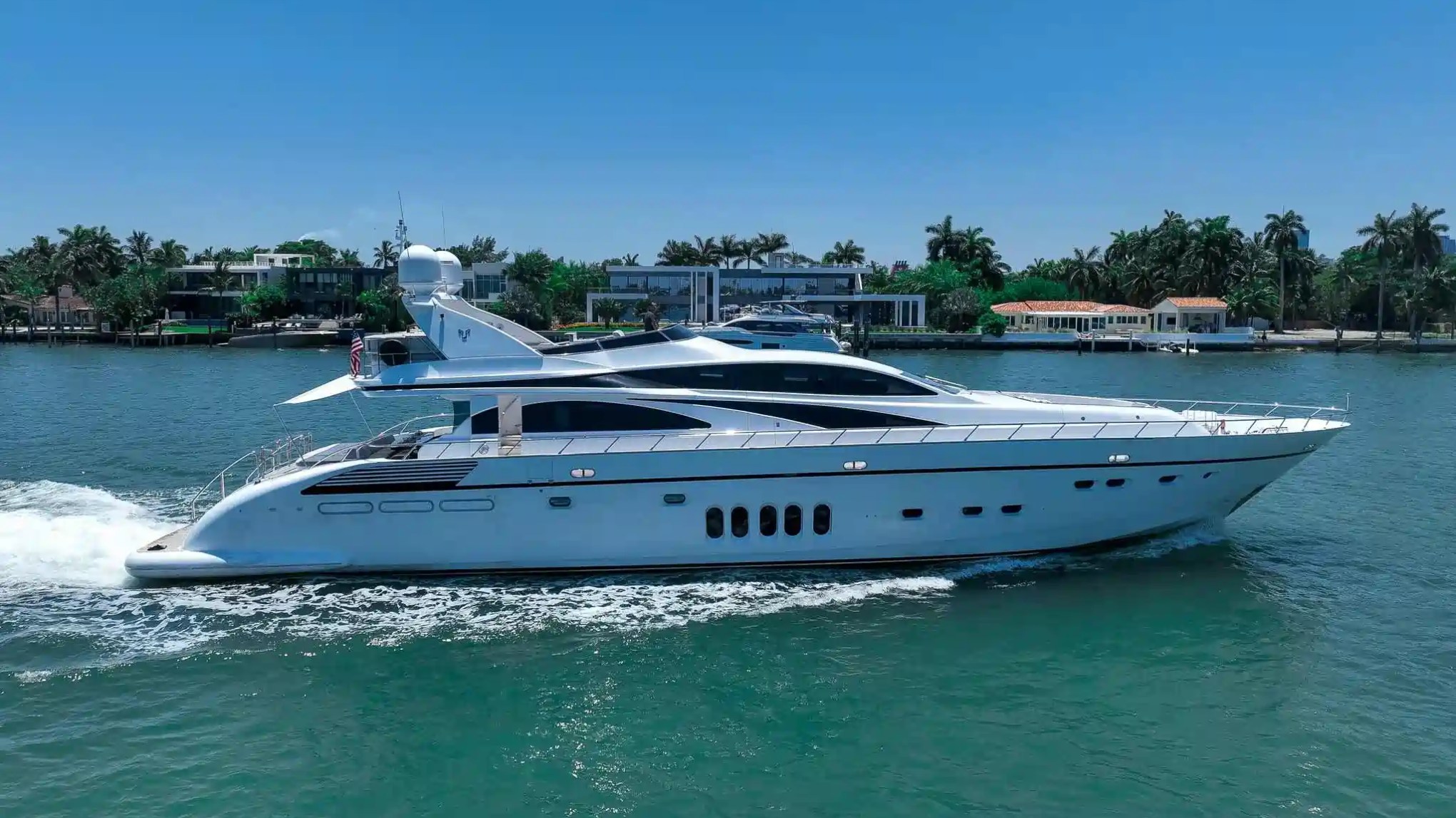 Luxurious white yacht cruising on a sunny day near waterfront homes.