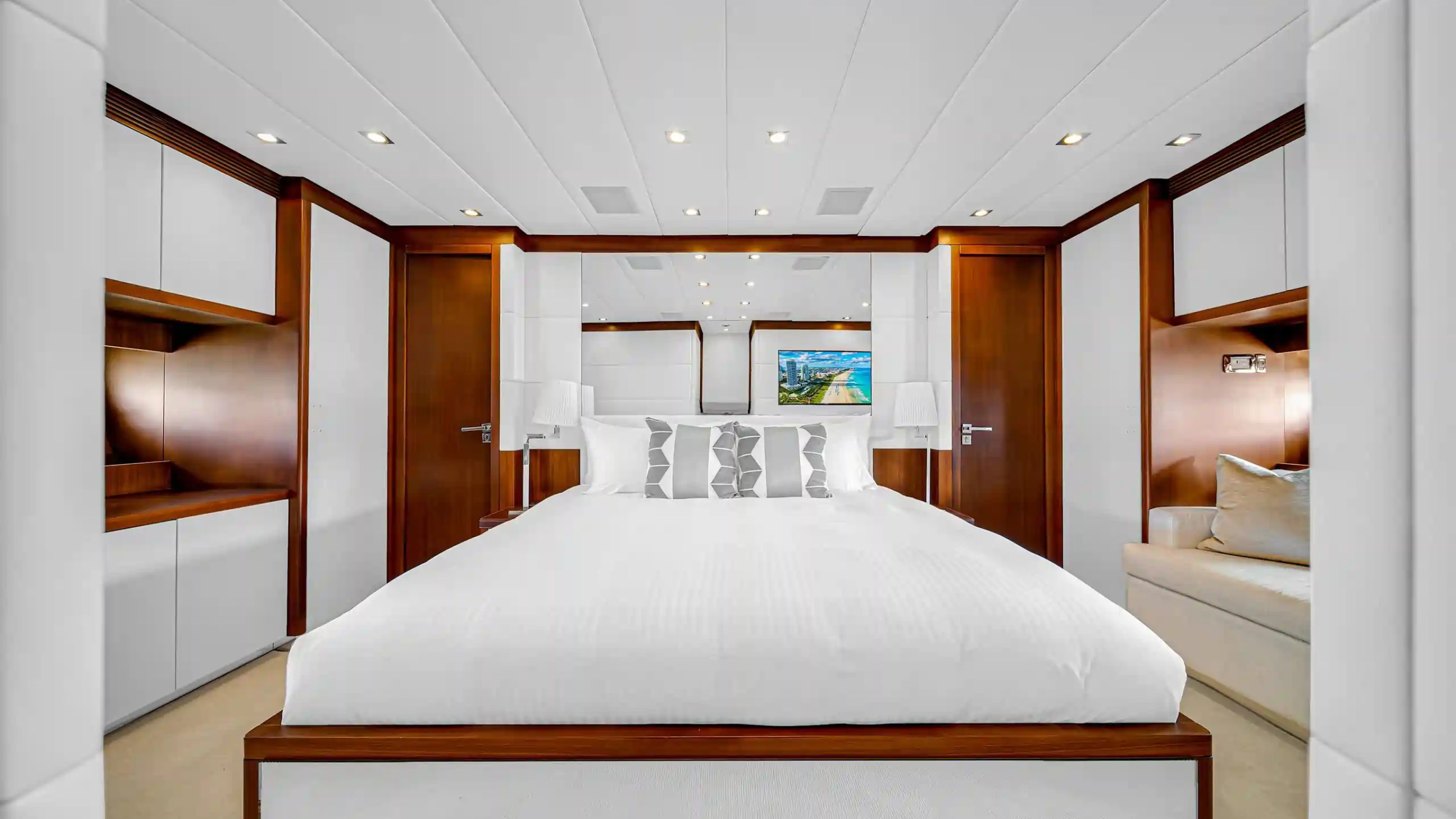 Modern bedroom with a large bed, white walls, wooden accents, and a wall-mounted TV.