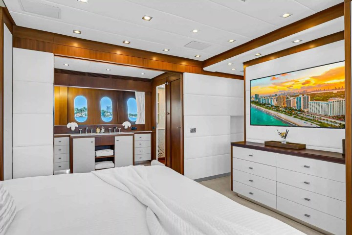 Luxurious yacht bedroom with wood accents, porthole windows, and cityscape TV display.