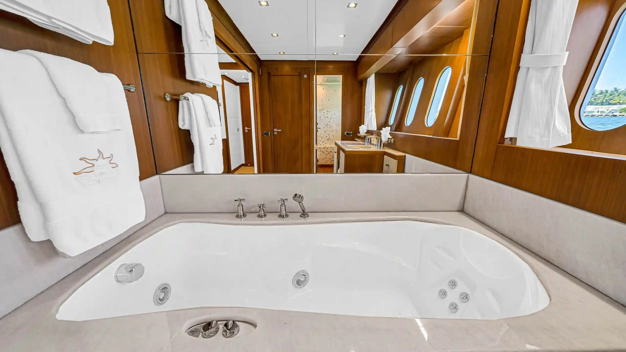 Luxury yacht bathroom with jacuzzi tub, mirrors, towels, and porthole windows.