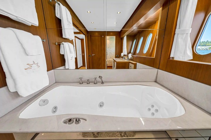 Luxury yacht bathroom with jacuzzi tub, mirrors, towels, and porthole windows.