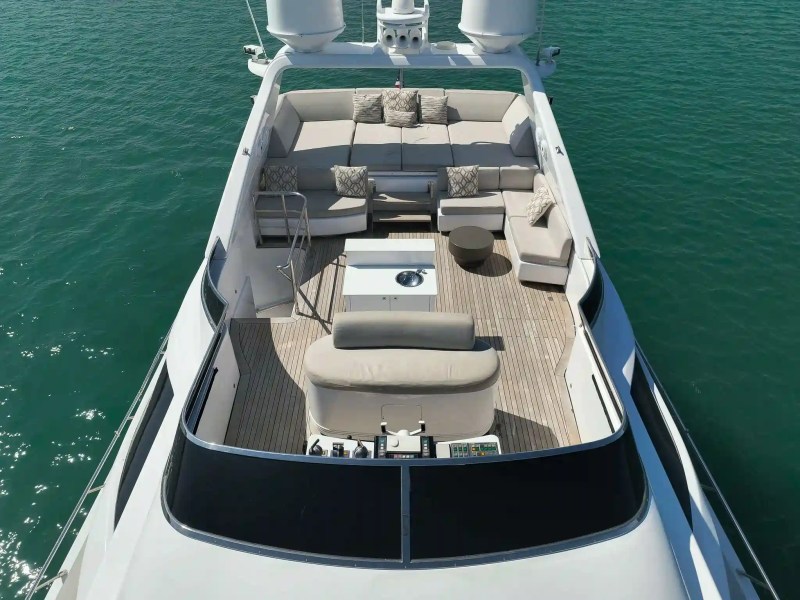 Aerial view of a yacht deck with sofas, cushions, and a table, surrounded by blue water.