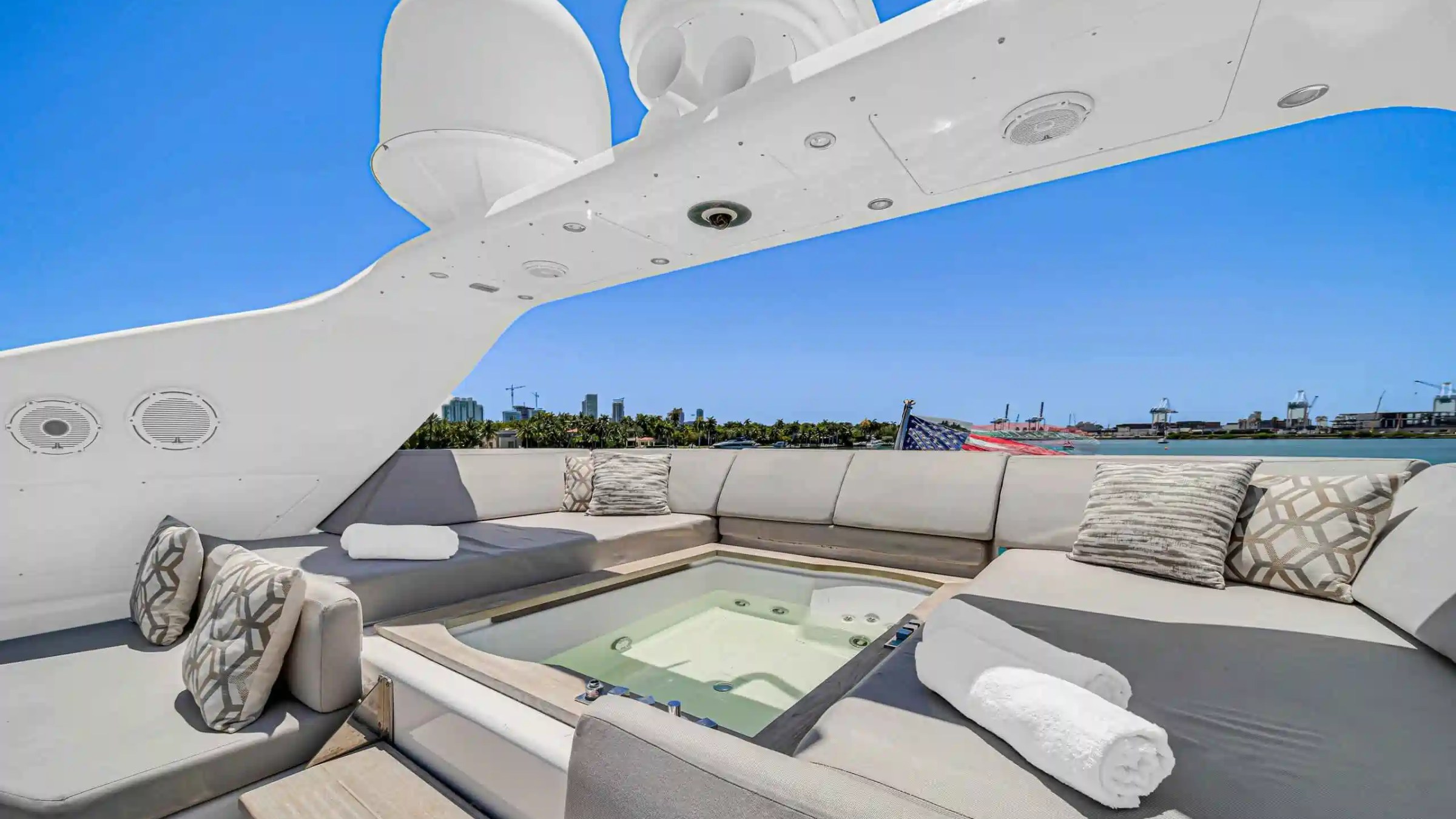Luxury yacht deck with jacuzzi, cushioned seating, and towel, set against a clear blue sky and waterfront view.