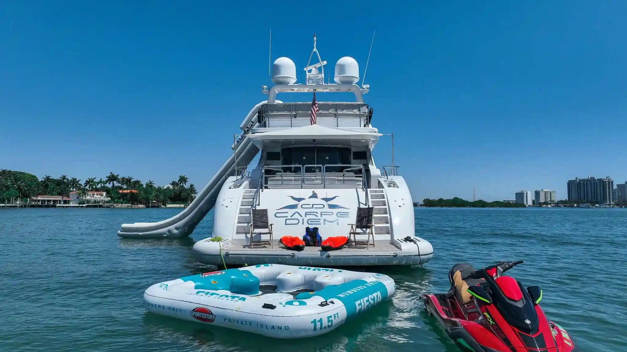 Large yacht on water with inflatable platform and jet ski nearby on a sunny day.