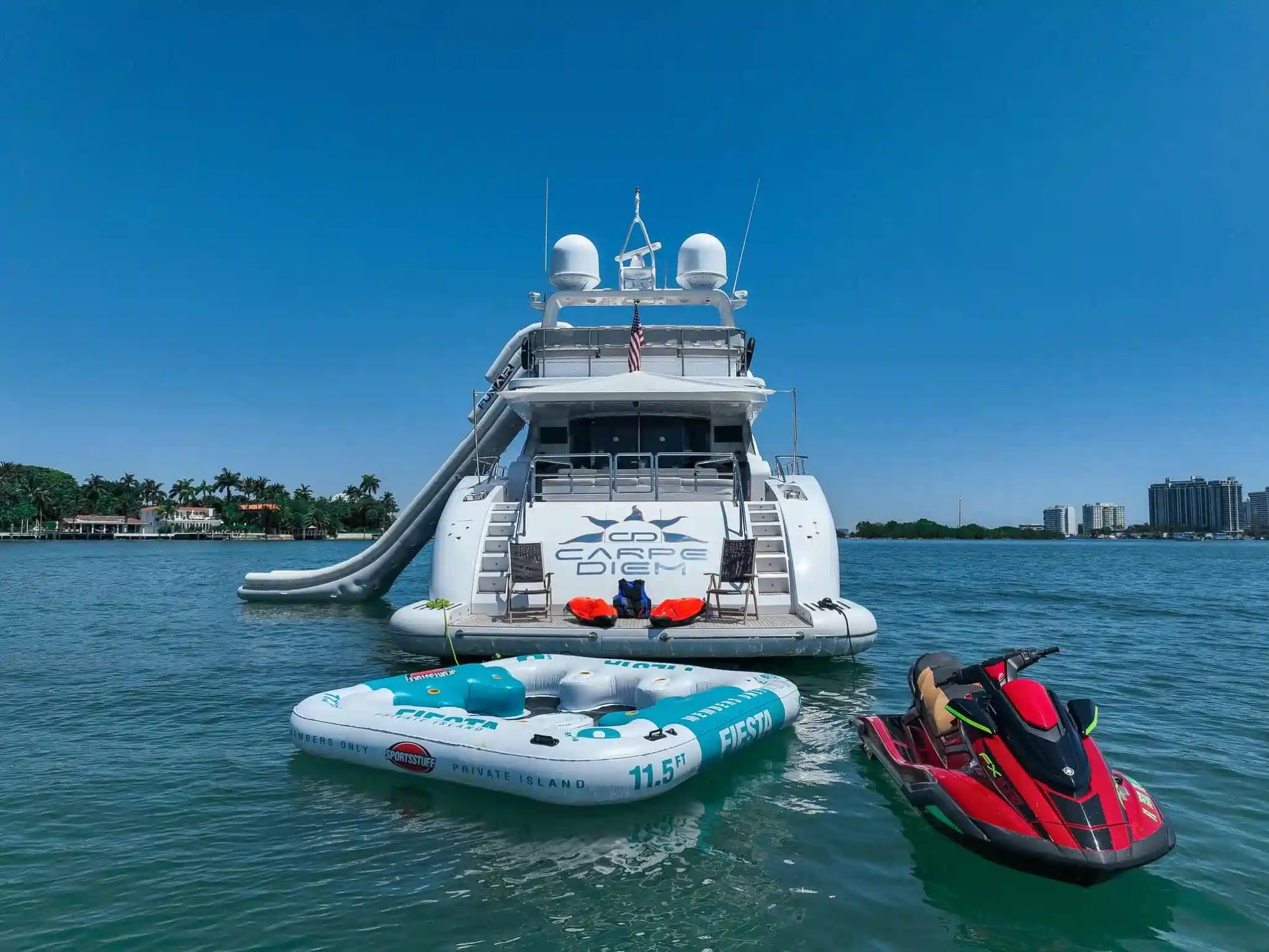 Large yacht on water with inflatable platform and jet ski nearby on a sunny day.