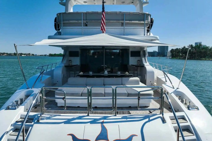 Rear deck of a luxury yacht with seating, canopy, and American flag on a sunny day.