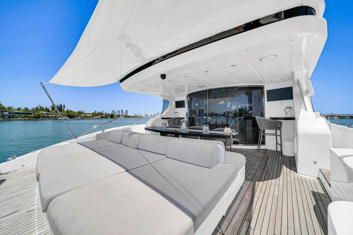 Spacious yacht deck with loungers, dining area, and city skyline in the background.