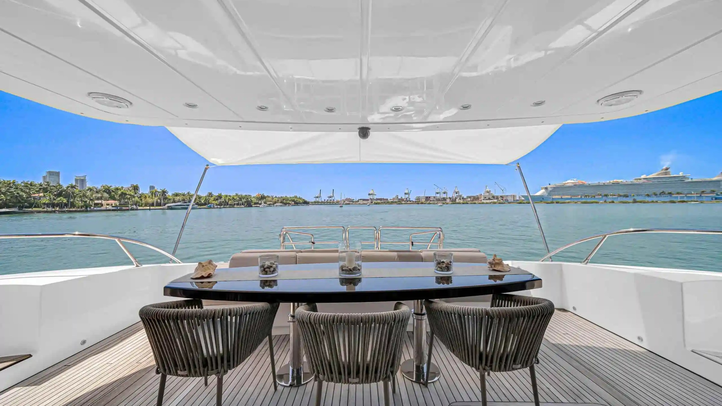 View from a yacht's deck with chairs and table overlooking calm water and a city skyline.