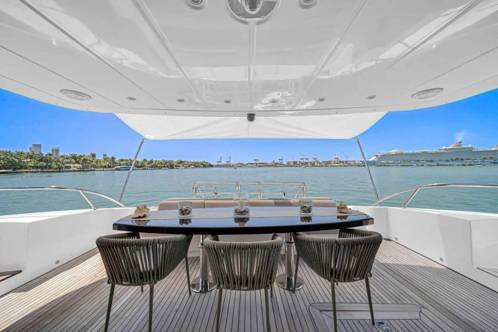 View from a yacht's deck with chairs and table overlooking calm water and a city skyline.