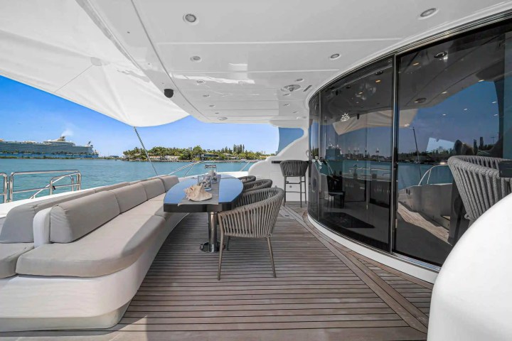 Luxury yacht deck with sofas, table, and ocean view; cruise ship and islands in background.