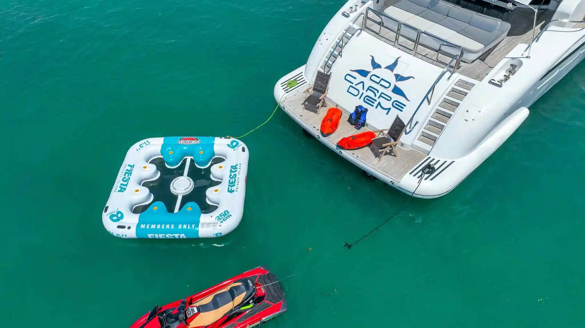 Yacht with inflatables and jet ski on turquoise water, aerial view.