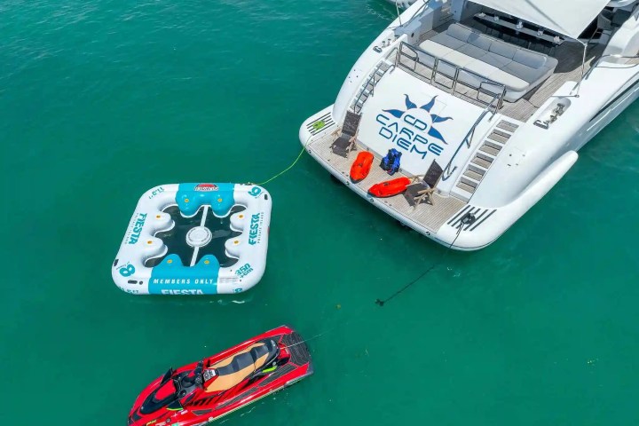 Yacht with inflatables and jet ski on turquoise water, aerial view.