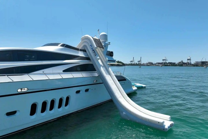 Luxury yacht with an inflatable slide leading into the ocean on a clear day.
