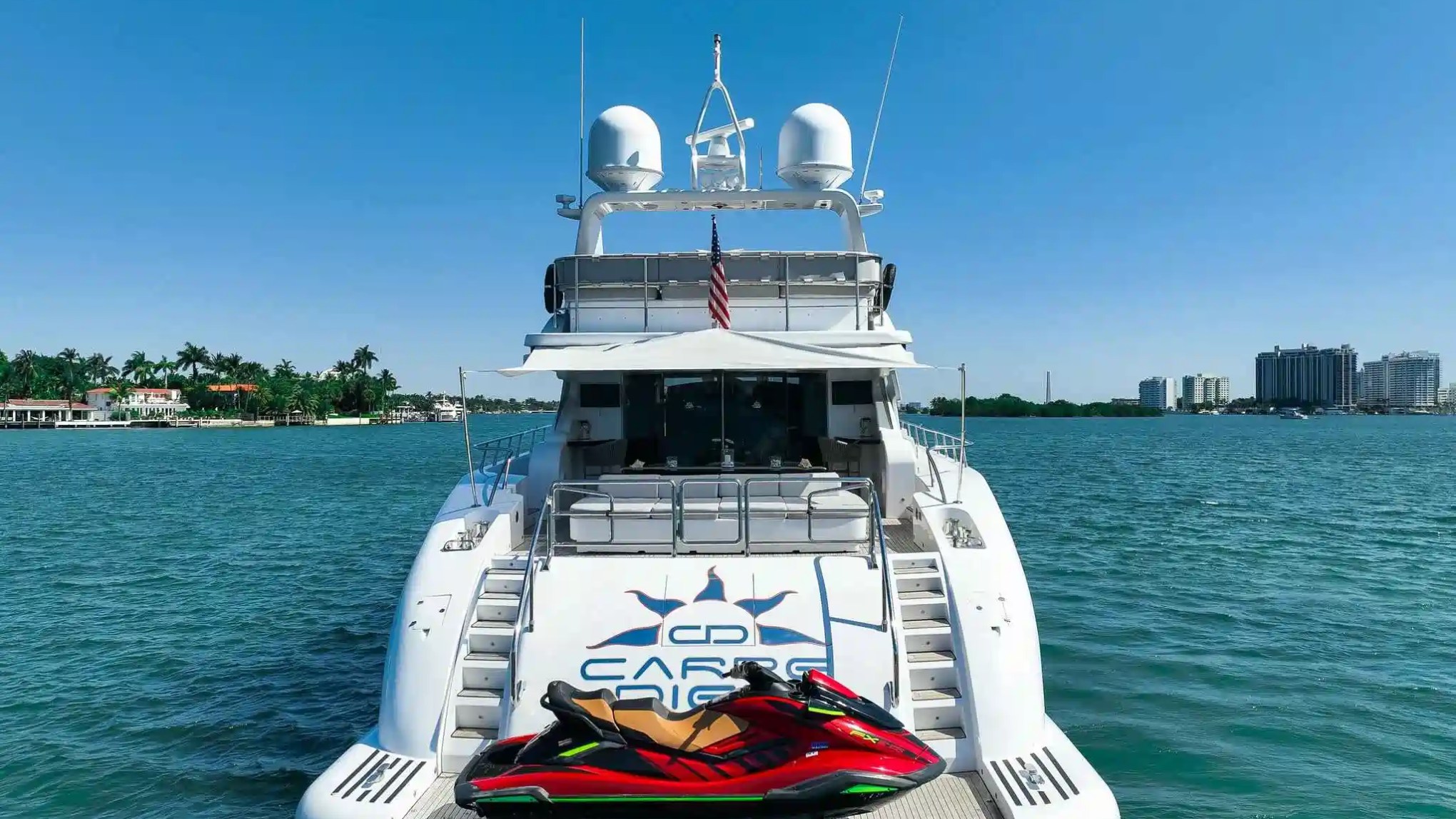 Rear view of a white yacht with jet skis on a blue water background.