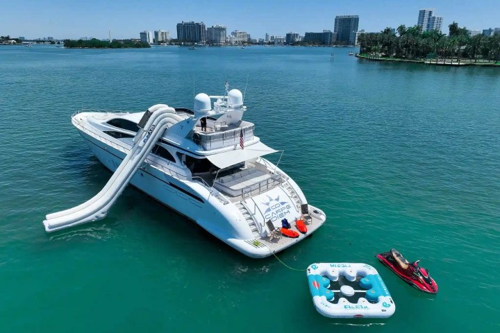 Yacht on water with inflatable slide, floating lounges, and jet ski nearby.