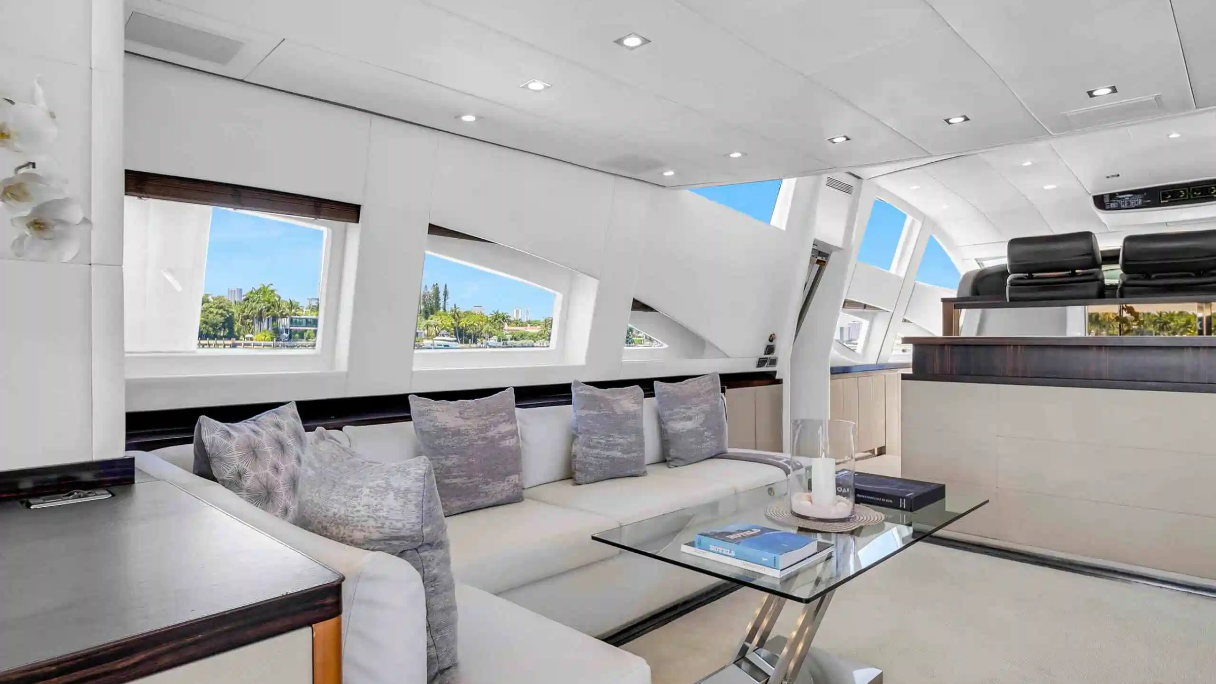 Modern yacht interior with white sofas, glass table, large windows, and view of the ocean.