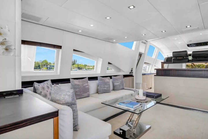 Modern yacht interior with white sofas, glass table, large windows, and view of the ocean.