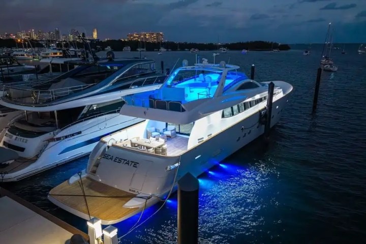 Luxury yacht docked at night with blue lights in a marina.