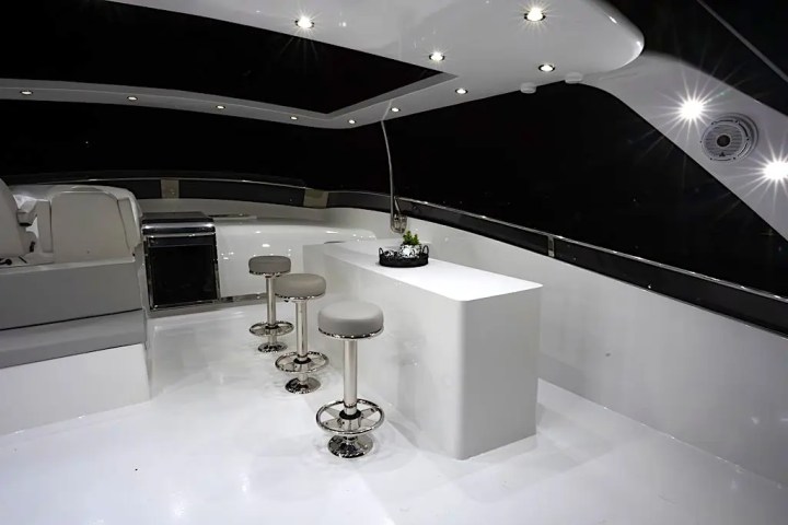 Interior of a modern boat featuring a sleek white bar and four bar stools under bright ceiling lights.