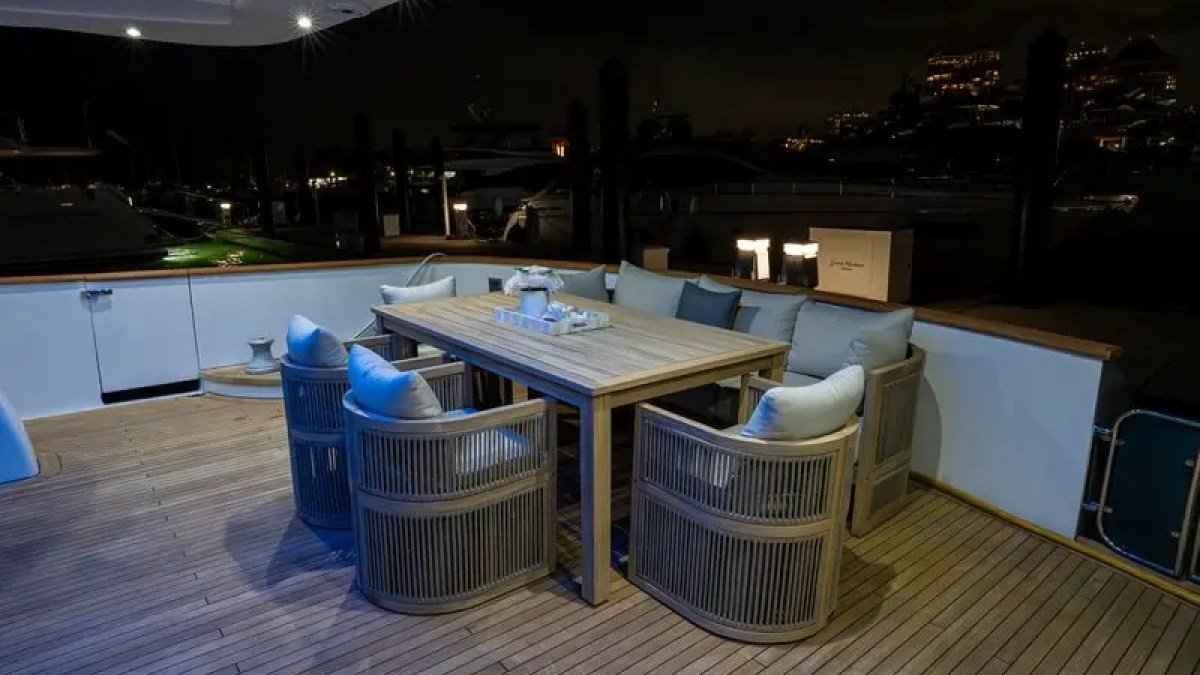 Wooden deck with table and wicker chairs on a yacht at night, softly lit.