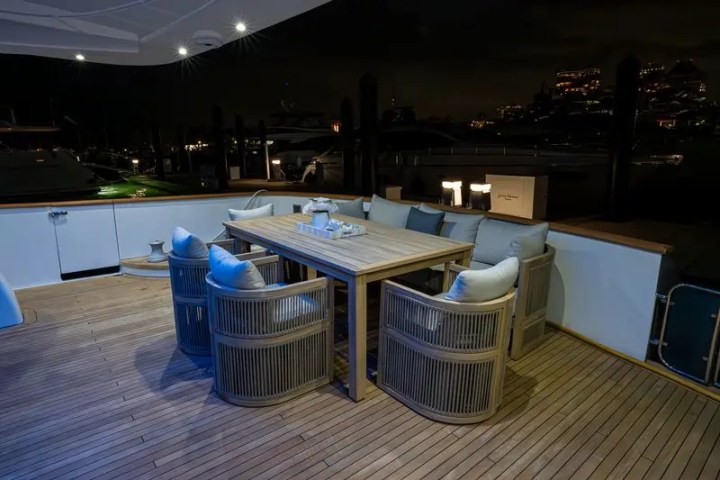 Wooden deck with table and wicker chairs on a yacht at night, softly lit.